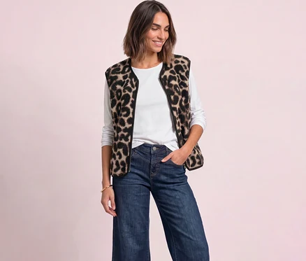Lächelnde Frau in einer Street One Leo-Weste, weißem Langarmshirt und blauen Jeans, mit der Hand in der Tasche.