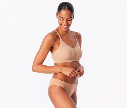 Lächelnde Frau trägt ein SCHIESSER Invisible Bustier mit Pads in Maple und passende Slips.