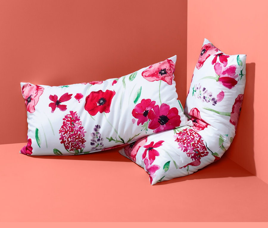 Zwei Renforcé-Kopfkissenbezüge mit Blumenmuster liegen in einer Ecke.