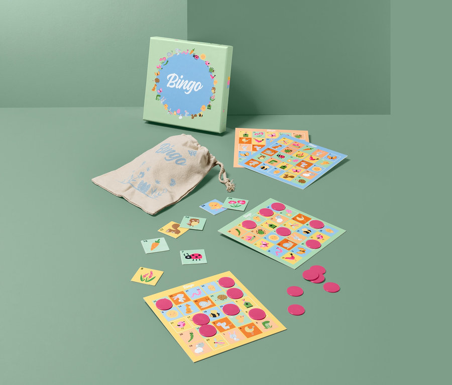 Ausgebreitetes Brettspiel »Osterbingo« mit Karten, Chips und Beutel auf grünem Hintergrund.