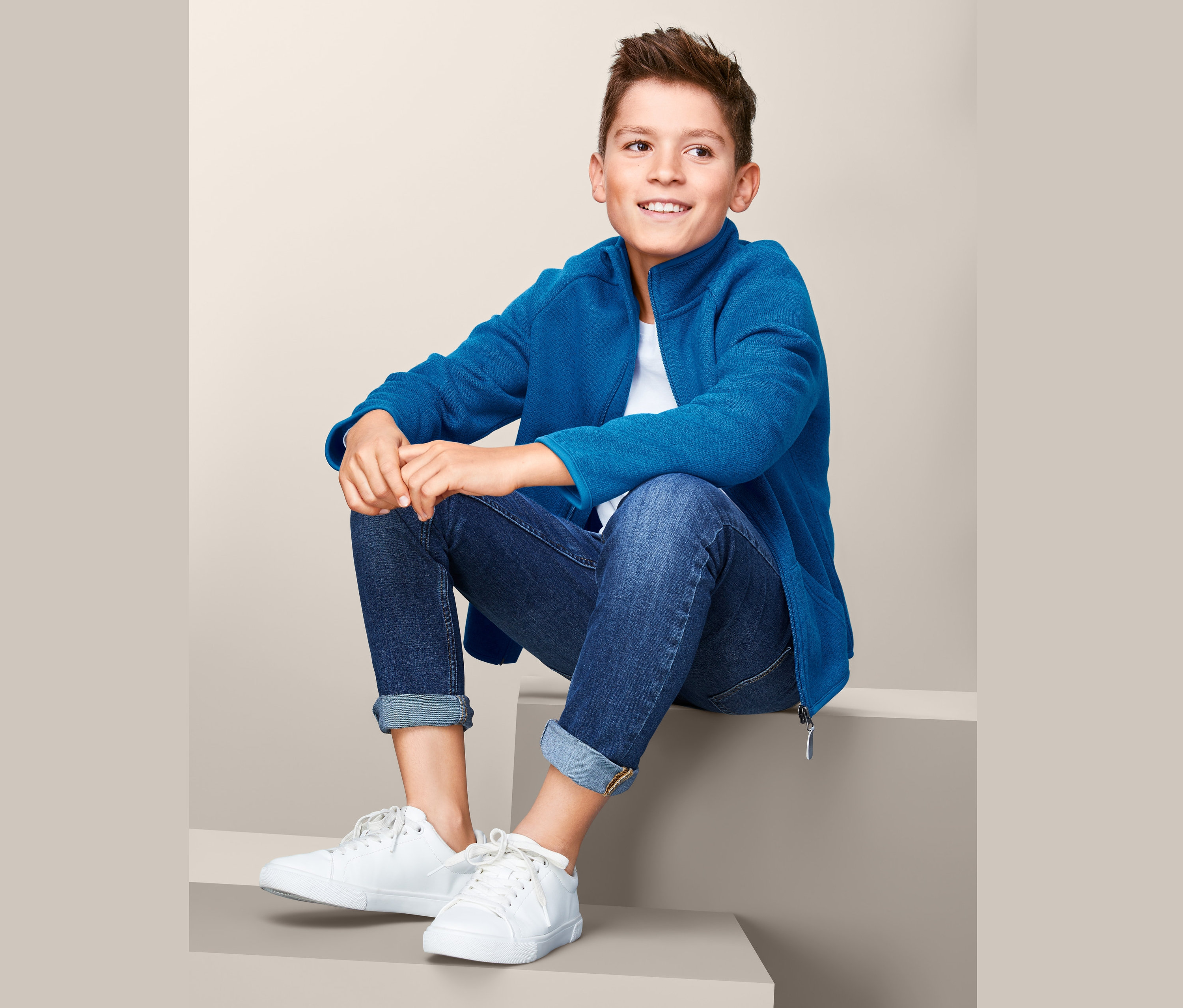 Junge sitzt auf Stufen und trägt eine Strickfleece-Jacke.