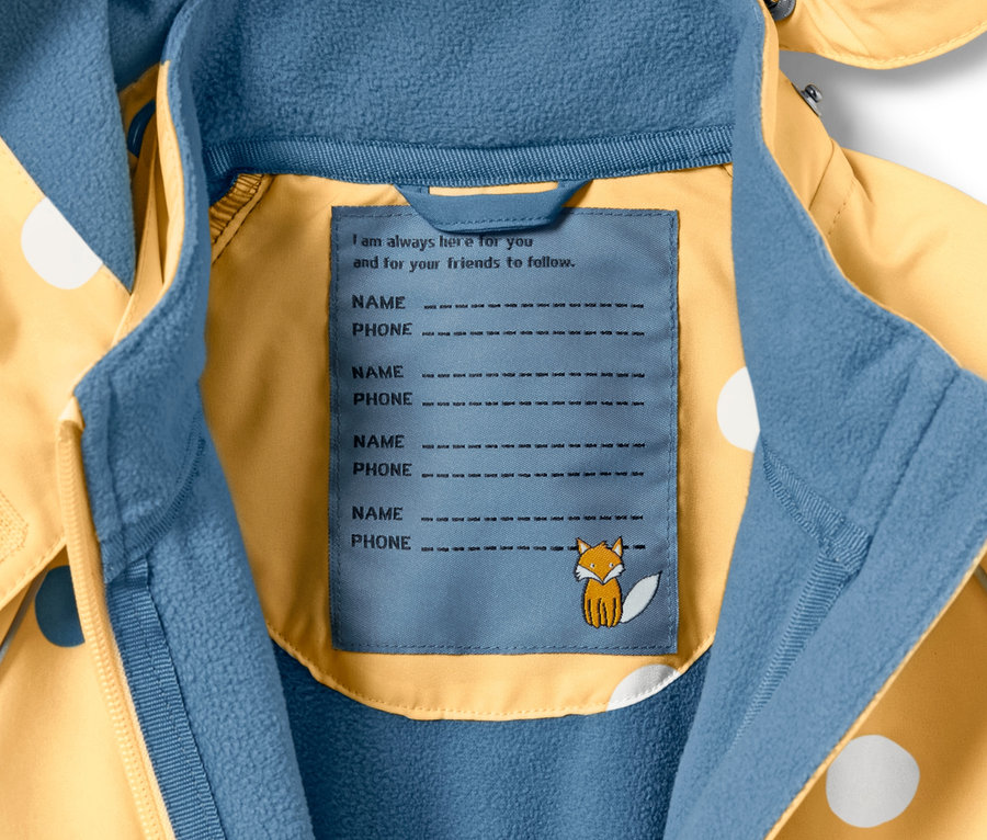 Detailansicht eines Kleinkind-Softshell-Einteilers mit Punkte-Alloverprint und Etikett für Name und Telefonnummer.