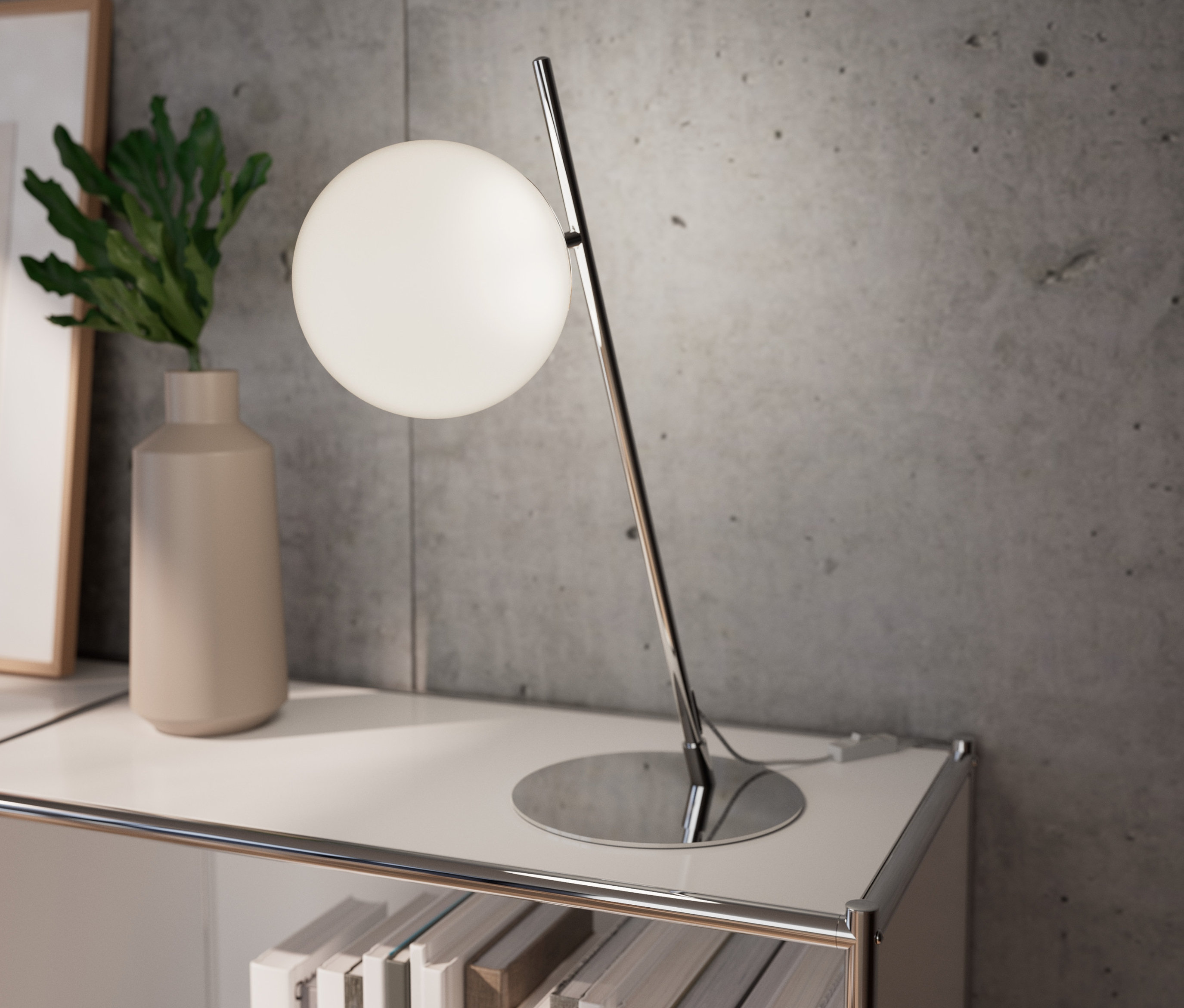 Eine verchromte Tischleuchte aus Metall steht auf einem weißen Regal neben einer Vase mit einer Pflanze.