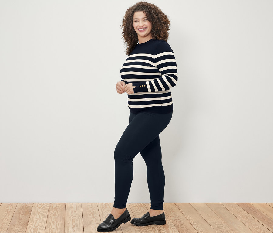 Frau posiert in dunkelblauem gestreiften Feinstrickpullover und schwarzen Heavy-Leggings.