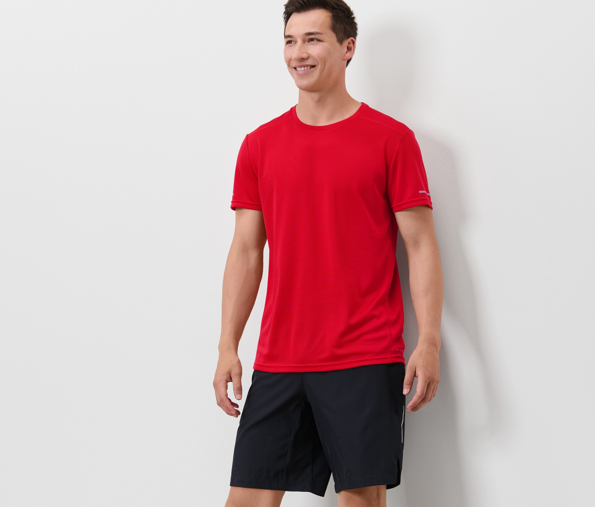 Mann steht und trägt ein rotes Funktionsshirt und schwarze Shorts.