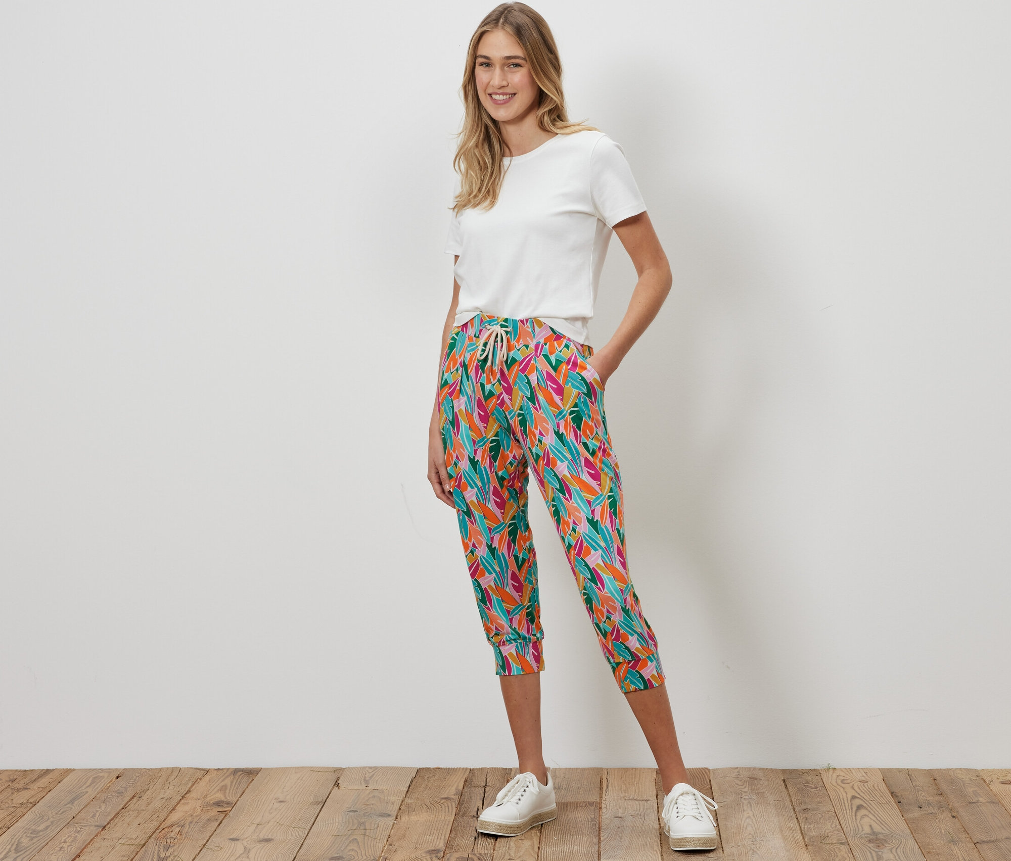 Frau steht und trägt eine mehrfarbige 3/4-Jerseyhose und ein weißes T-Shirt.
