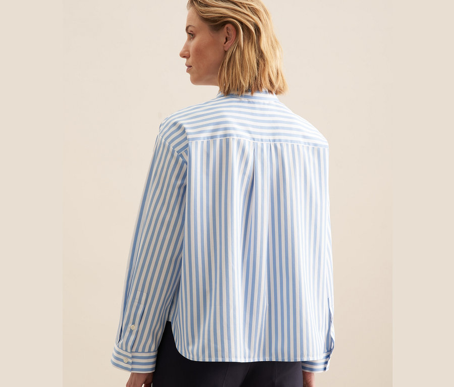 Rückansicht einer blonden Frau, die eine blaue Seidensticker Oversize Hemdbluse trägt.