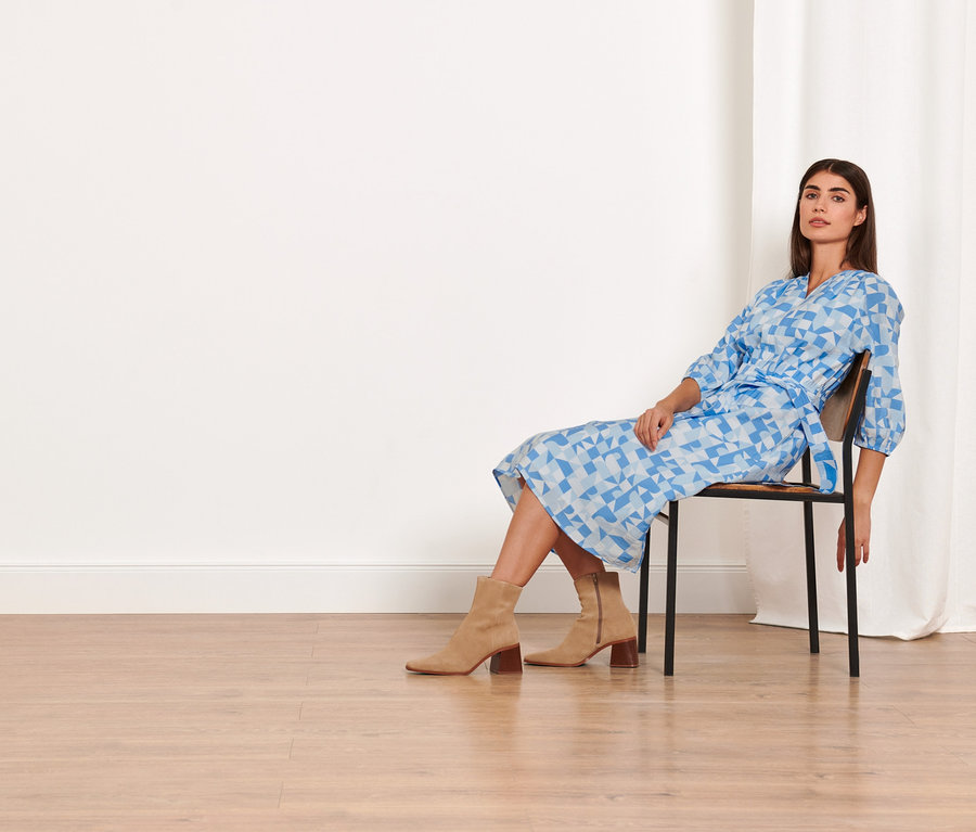 Frau sitzt auf einem Stuhl und trägt ein bedrucktes Webkleid.