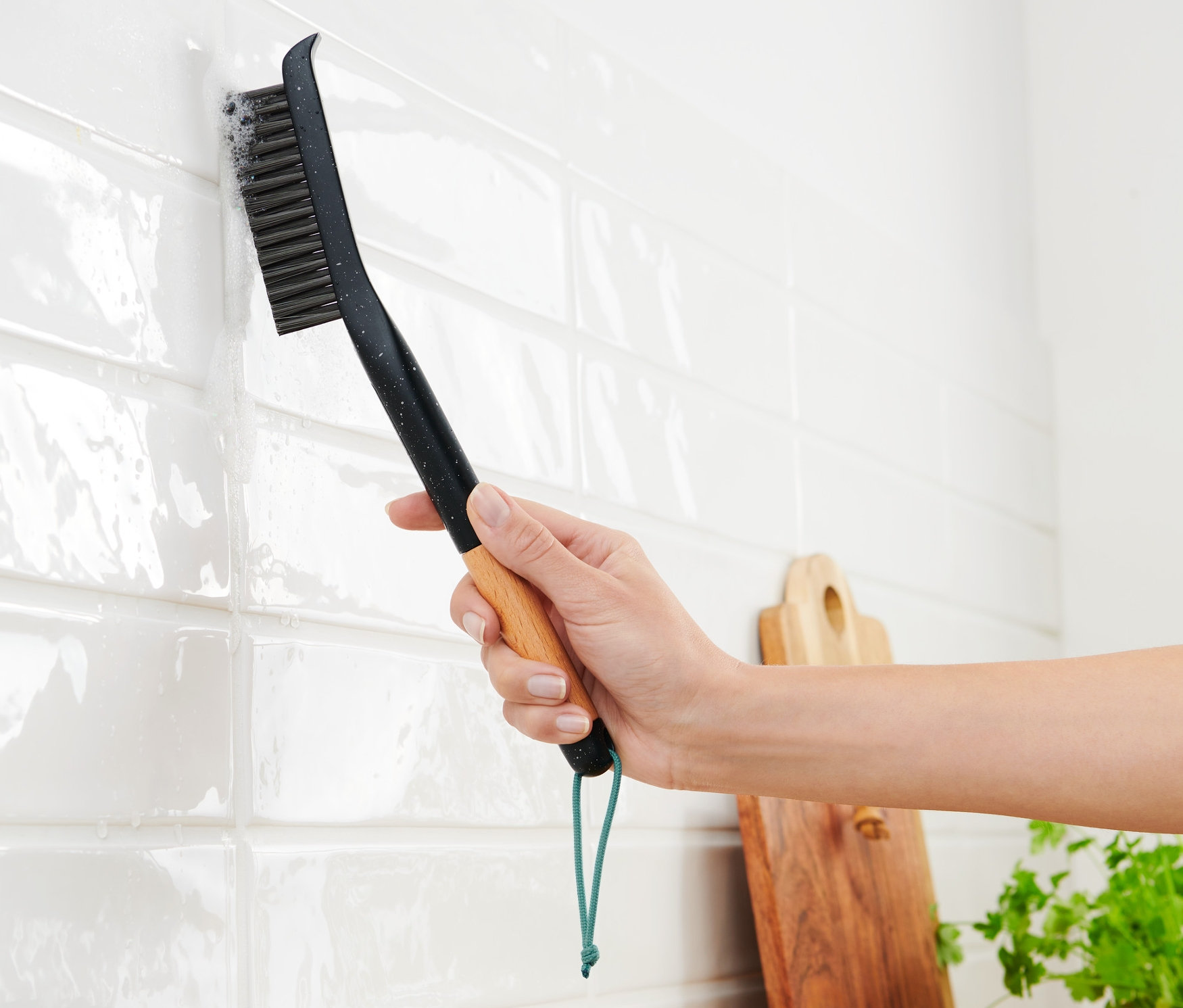 Frau putzt weiße Fliesen mit einer langen Fugenbürste.