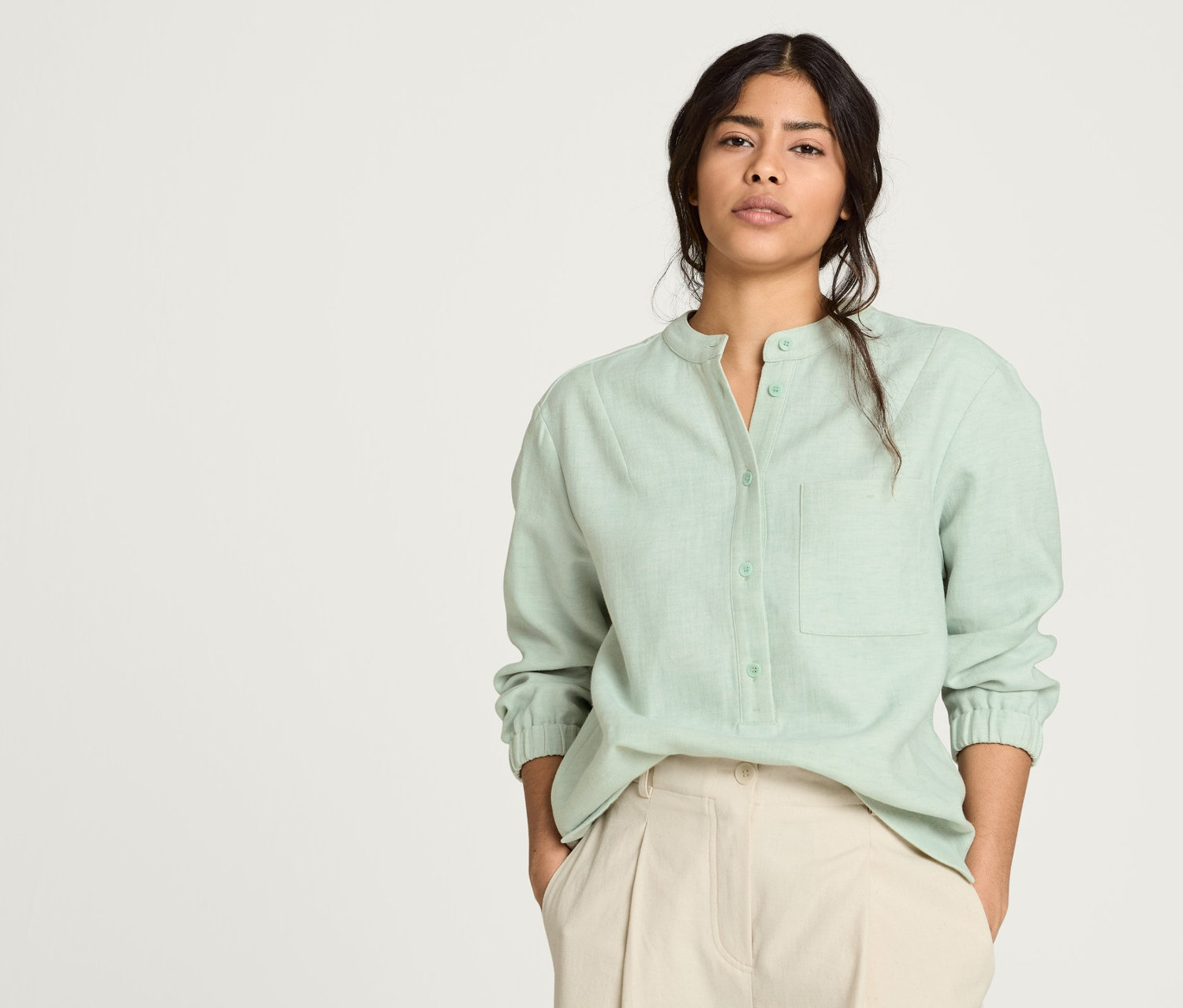 Frau posiert in einer grünen NAH/STUDIO Bluse aus Baumwoll-Leinen-Mix und einer ungefärbten NAH/STUDIO Barrel-Hose aus Baumwolle.