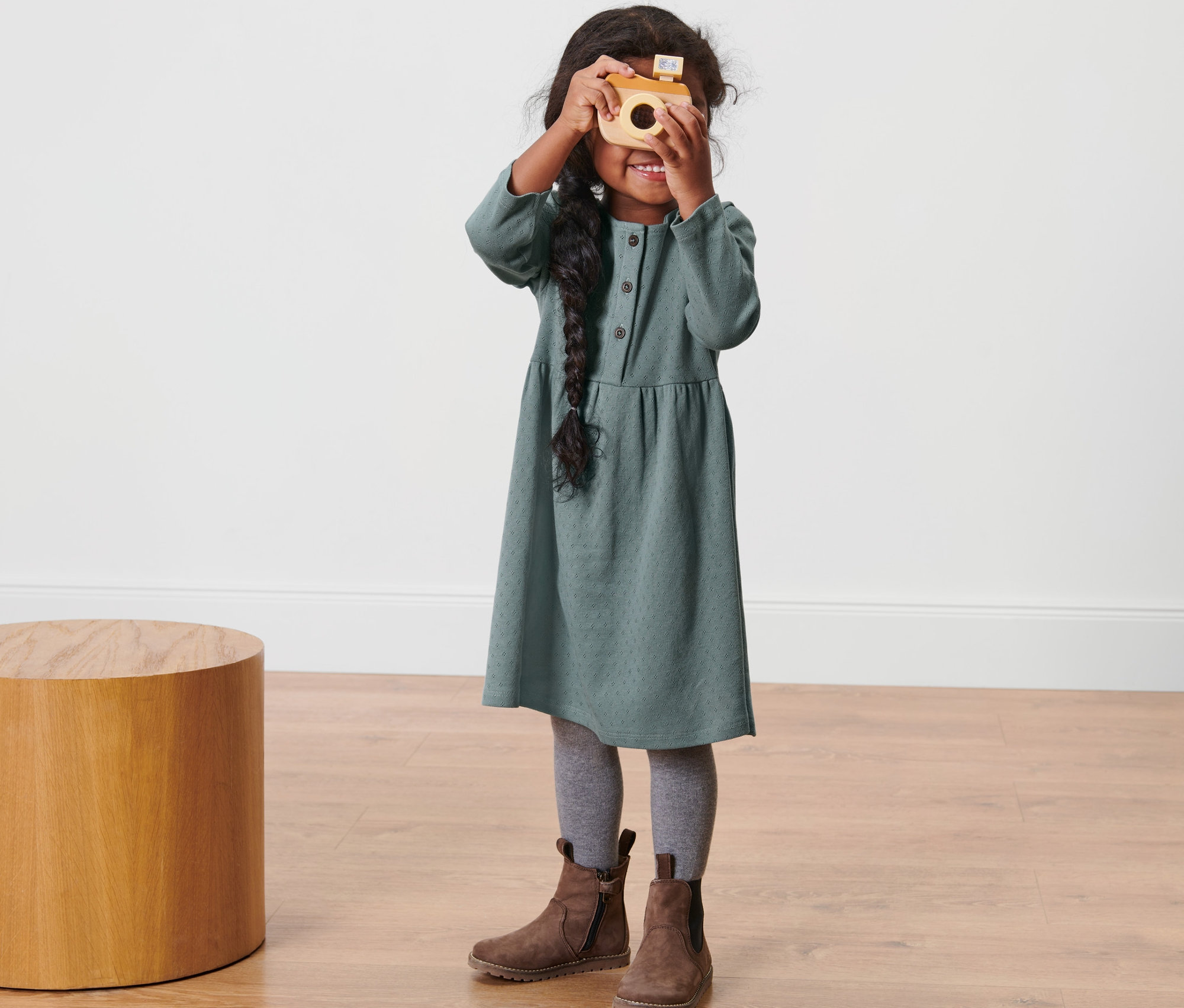 Mädchen im Kleinkind-Kleid hält eine Holzkamera vor ihr Gesicht.