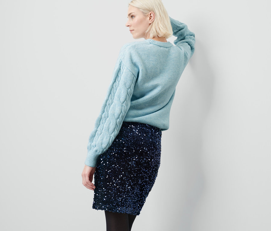 Frau posiert in Pullover und Paillettenrock.