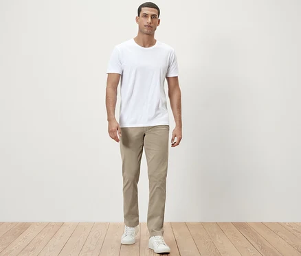 Mann steht in weißem T-Shirt und beiger Chino.