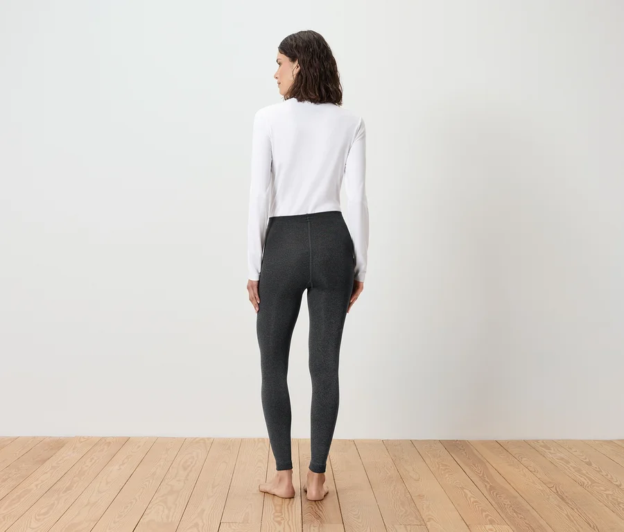 Frau steht mit dem Rücken zur Kamera und trägt ein weißes Langarmshirt und graue Leggings.