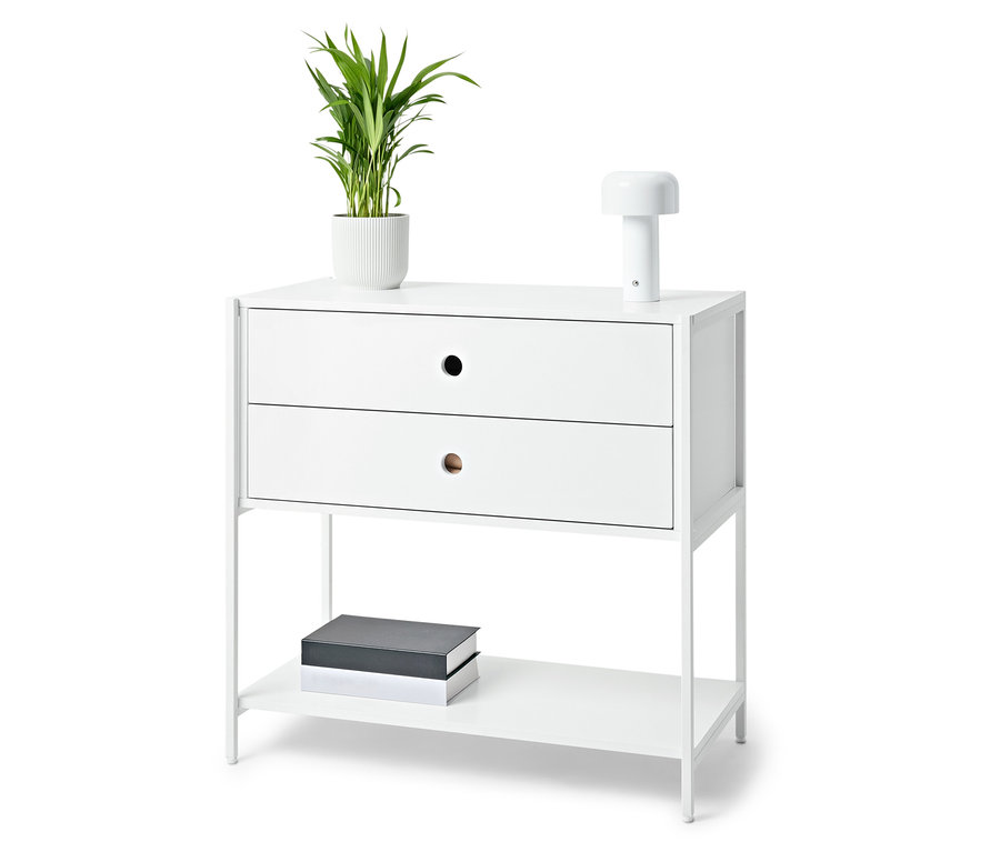 Weißer Nachttisch mit zwei Schubladen, Lampe, Topfpflanze und Büchern.