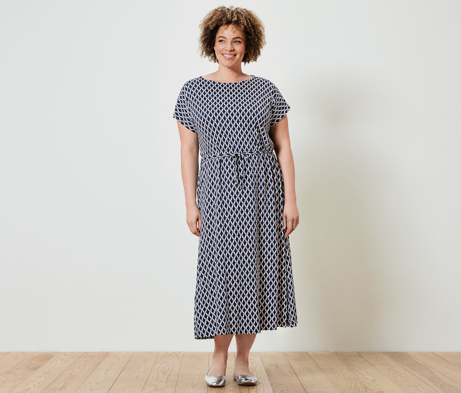 Frau steht und trägt ein bedrucktes Jerseykleid.