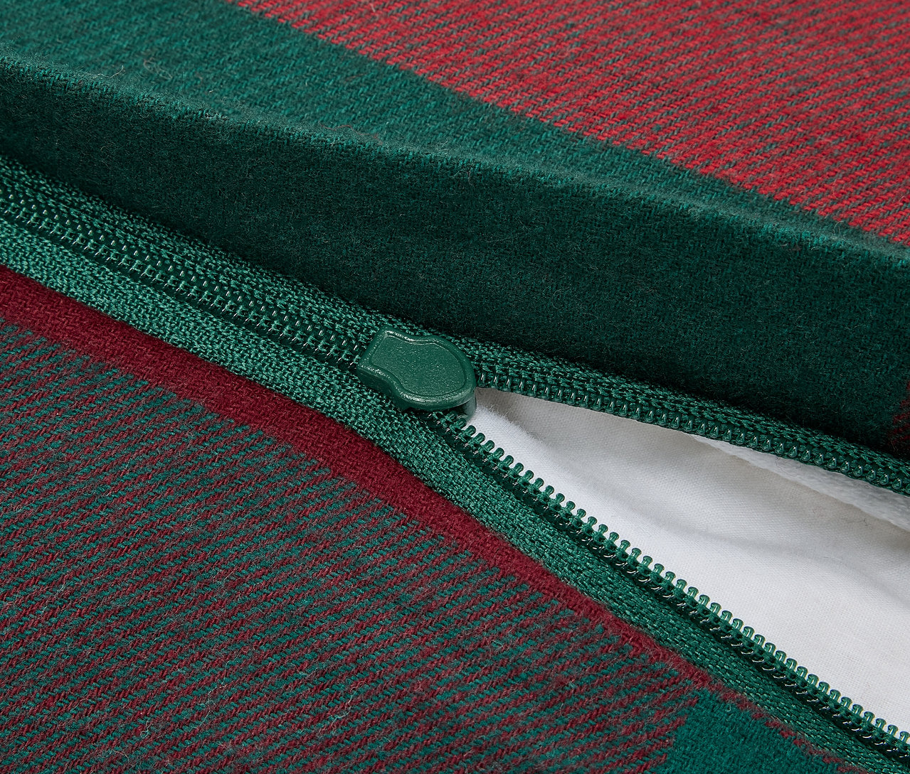 Nahaufnahme eines Reißverschlusses eines grün-rot karierten Kissenbezugs, der eine weiße Innenfüllung freilegt.