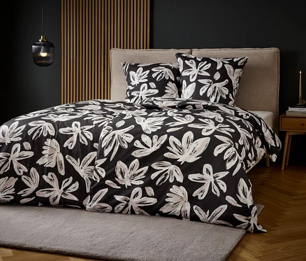 Bett mit schwarz-weißem Blumenmuster-Bettzeug auf grauem Teppich.