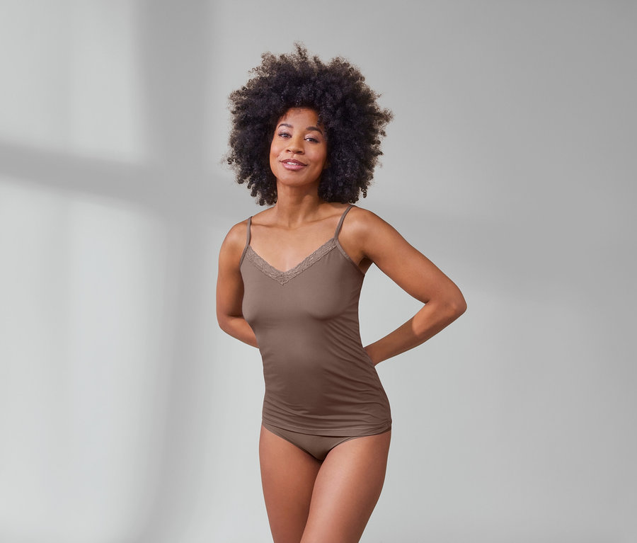 Frau mit Afro trägt ein nougatfarbenes Hemdchen und 5 beige Magic-Cut-Pantys.