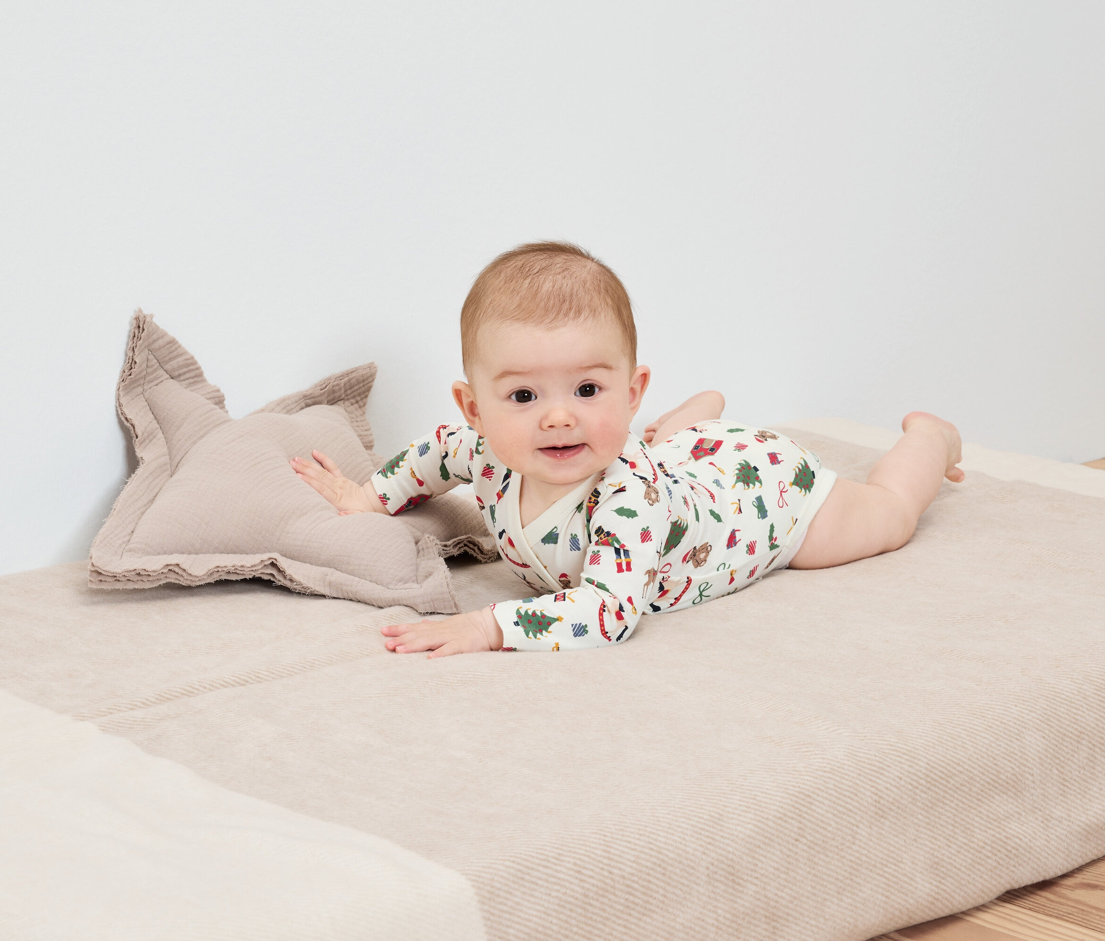 Baby liegt auf dem Bauch auf einer Decke neben einem sternförmigen Kissen.