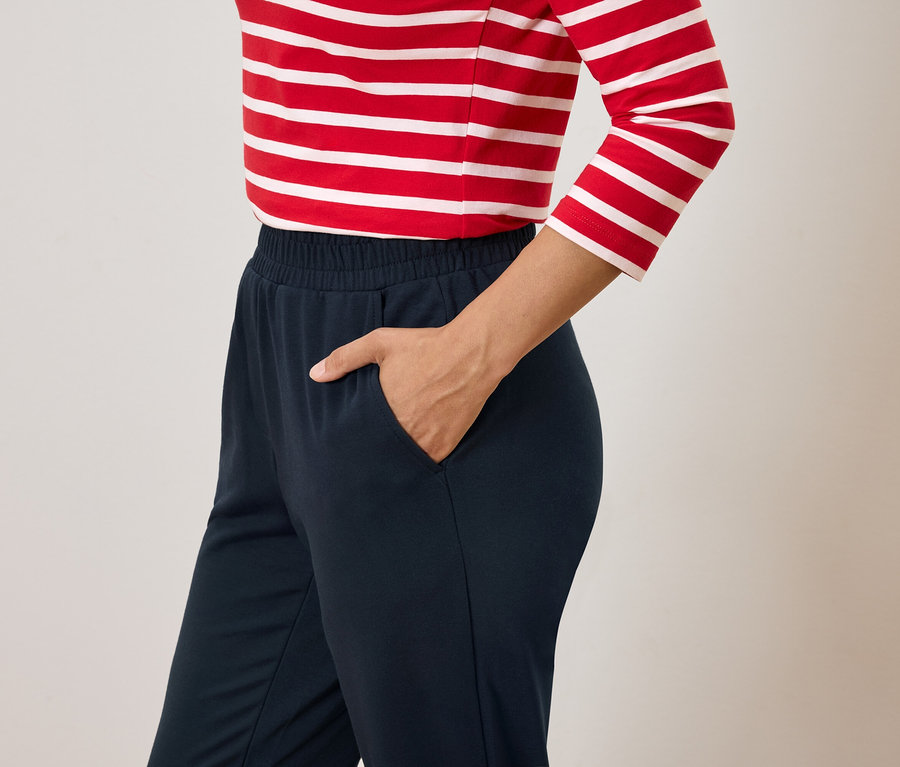 Frau mit Hand in der Tasche einer dunkelblauen Hose und rot-weiß gestreiftem Oberteil.