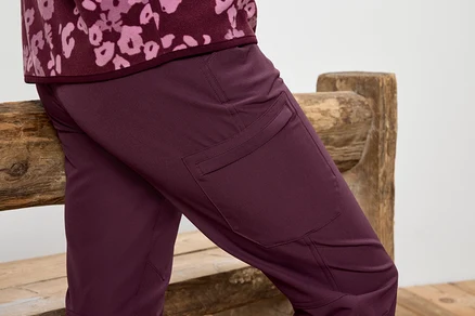 Weinrote Hose mit Oberschenkeltaschen, die an einer Holzbank lehnt.
