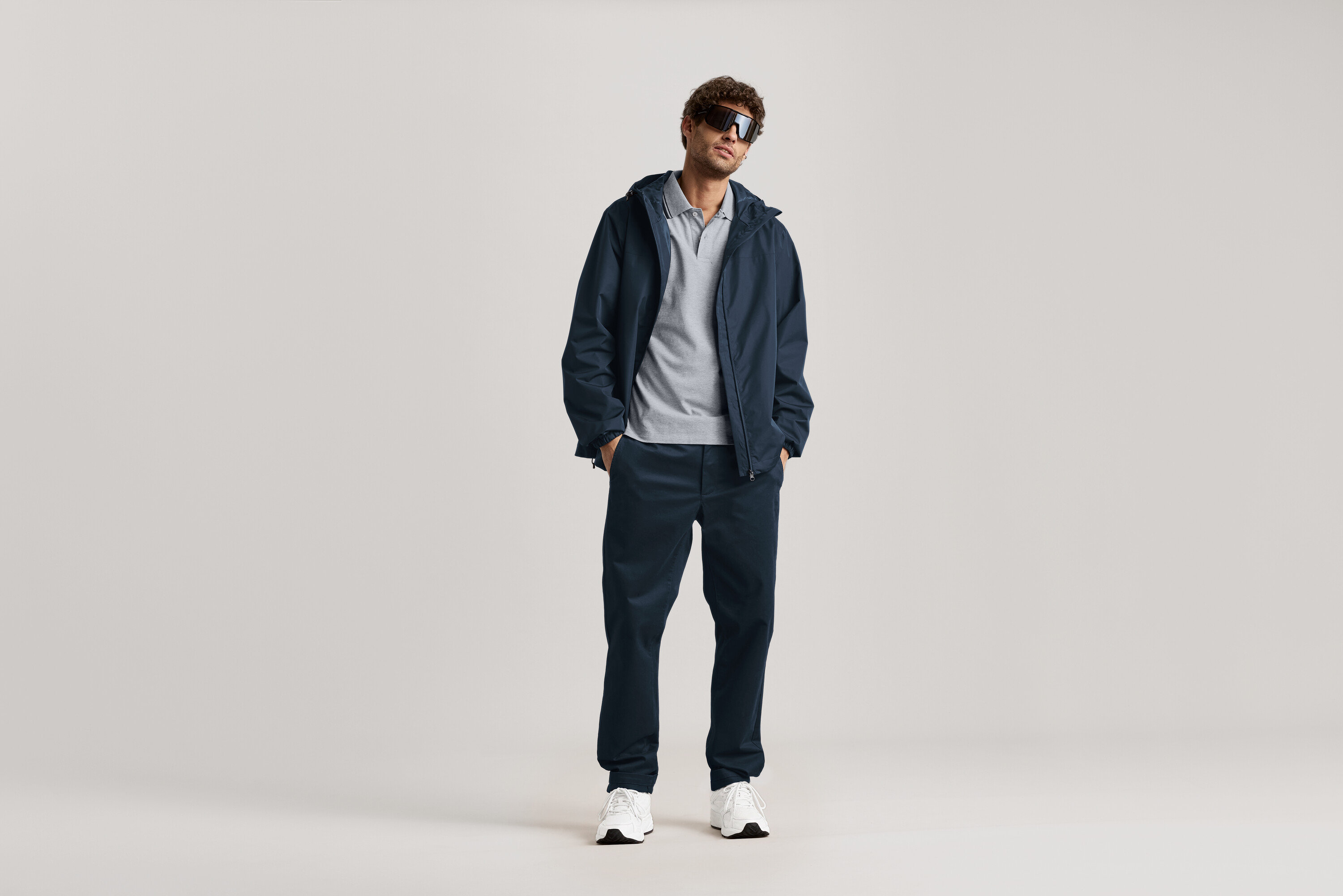 Ein Mann steht mit Sonnenbrille, marineblauer Jacke und marineblauer Chino.