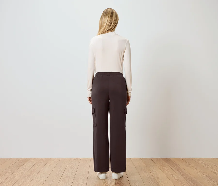 Rückansicht einer Frau mit blonden Haaren, die einen cremefarbenen Rollkragenpullover, braune Cargohose und weiße Turnschuhe trägt.