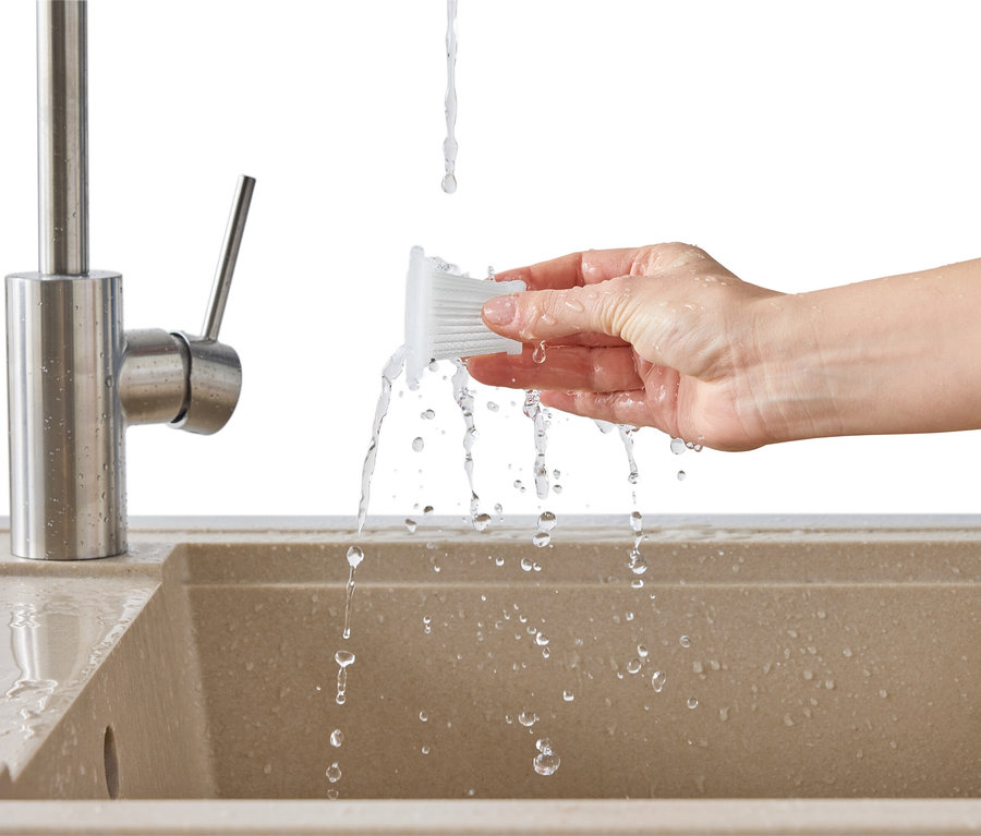 Eine Hand hält einen weißen Filter unter einen Wasserhahn über einem Spülbecken.