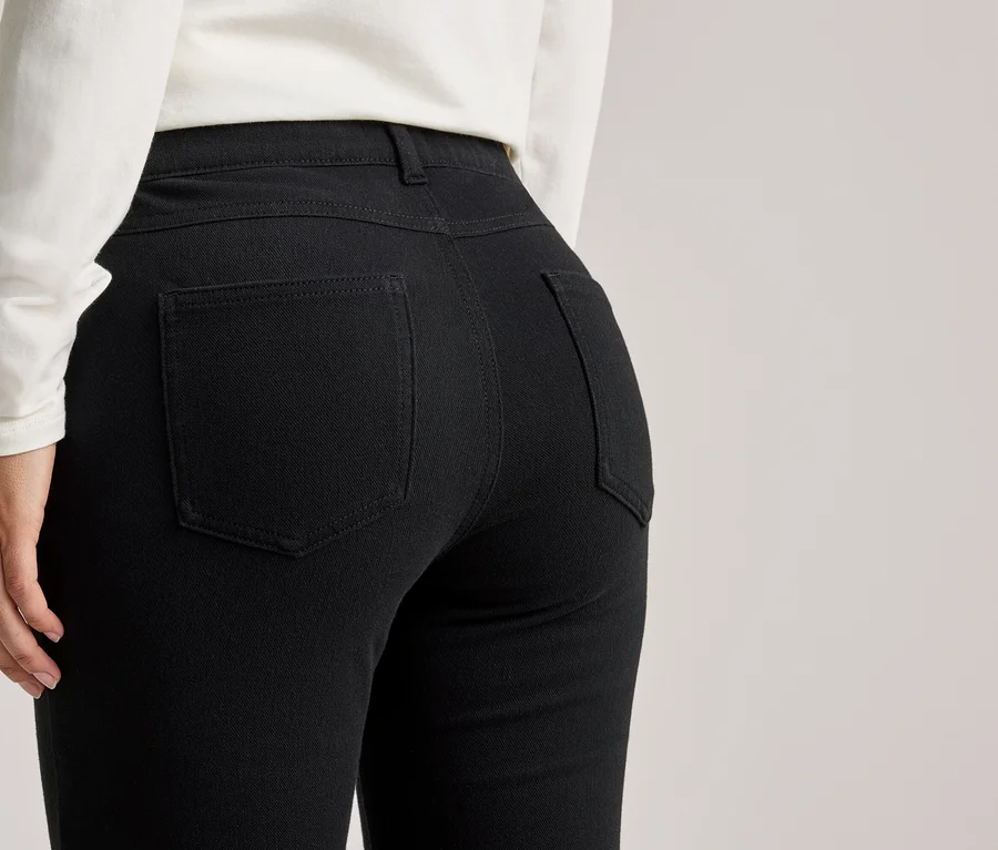 Rückansicht einer Frau mit weißem Oberteil und schwarzer Hose mit Gesäßtaschen.