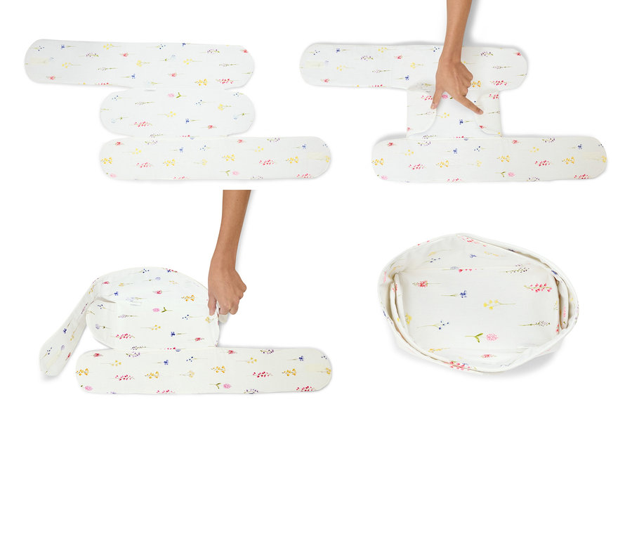 Hände falten eine weiße Babyliege mit Blumenmuster.