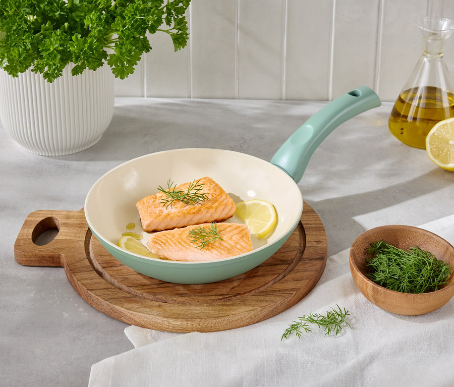 Zwei Lachsfilets mit Zitronenscheiben und Dill in einer hellen Pfanne auf einem Holzbrett.