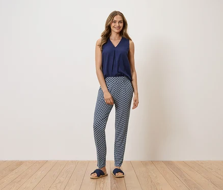 Frau steht und trägt ein marineblaues Top, gemusterte Hose und Sandalen.