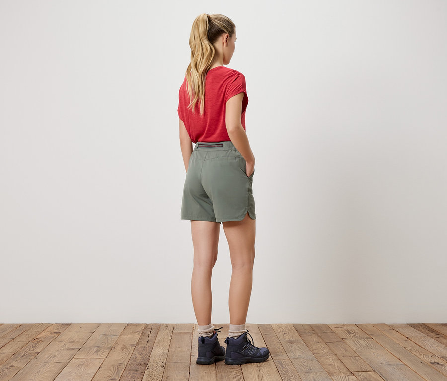 Frau von hinten in rotem T-Shirt, Shorts und Wanderschuhen.