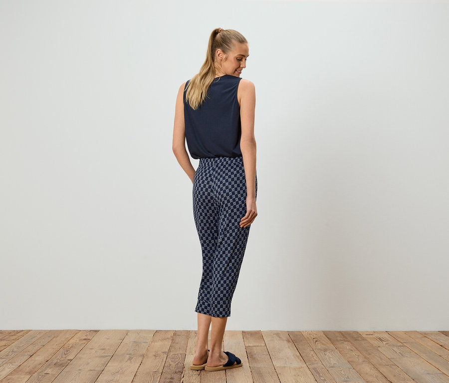 Frau mit blauem Top und gemusterter Hose, von hinten gesehen.