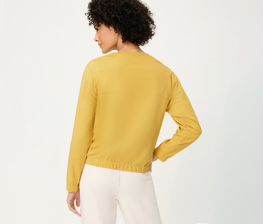 Frau von hinten mit Olsen Sweatjacke in Gelb und heller Hose.