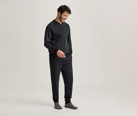 Mann mit dunkler Jacke und Hose, die Hände in den Taschen, graue Socken tragend.