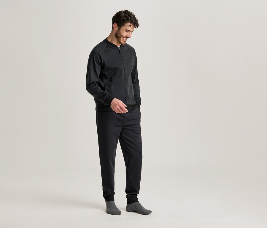 Mann mit dunkler Jacke und Hose, die Hände in den Taschen, graue Socken tragend.