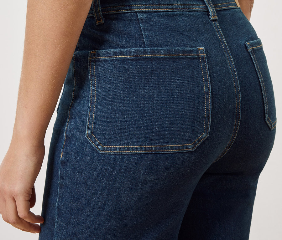 Nahaufnahme der Rückseite einer Person, die dunkelblaue Jeans mit aufgesetzten Gesäßtaschen trägt.