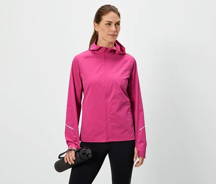 Frau hält eine schwarze Wasserflasche, trägt eine pinke Jacke und schwarze Leggings vor einem weißen Hintergrund.