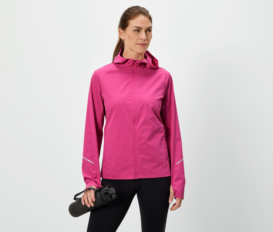 Frau hält eine schwarze Wasserflasche, trägt eine pinke Jacke und schwarze Leggings vor einem weißen Hintergrund.