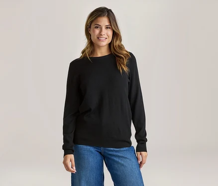Lächelnde Frau in schwarzem Langarmshirt und blauen Jeans.
