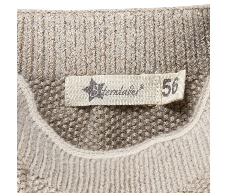 Nahaufnahme eines weißen Sterntaler-Etiketts mit der Größe 56, das auf eine beigefarbene Baby-Strickhose genäht ist.