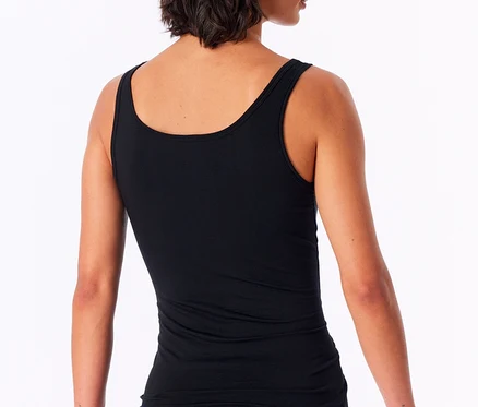 Eine Frau mit kurzen dunklen Haaren, von hinten leicht gedreht, trägt ein schwarzes SCHIESSER Trägertop mit Modal und Streifen sowie einen schwarzen Slip. Sie blickt über ihre rechte Schulter.