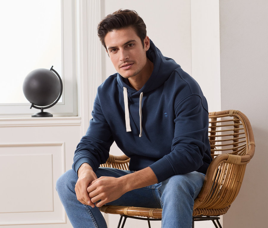 Mann sitzt im Sessel und trägt einen dunkelblauen Hoodie.