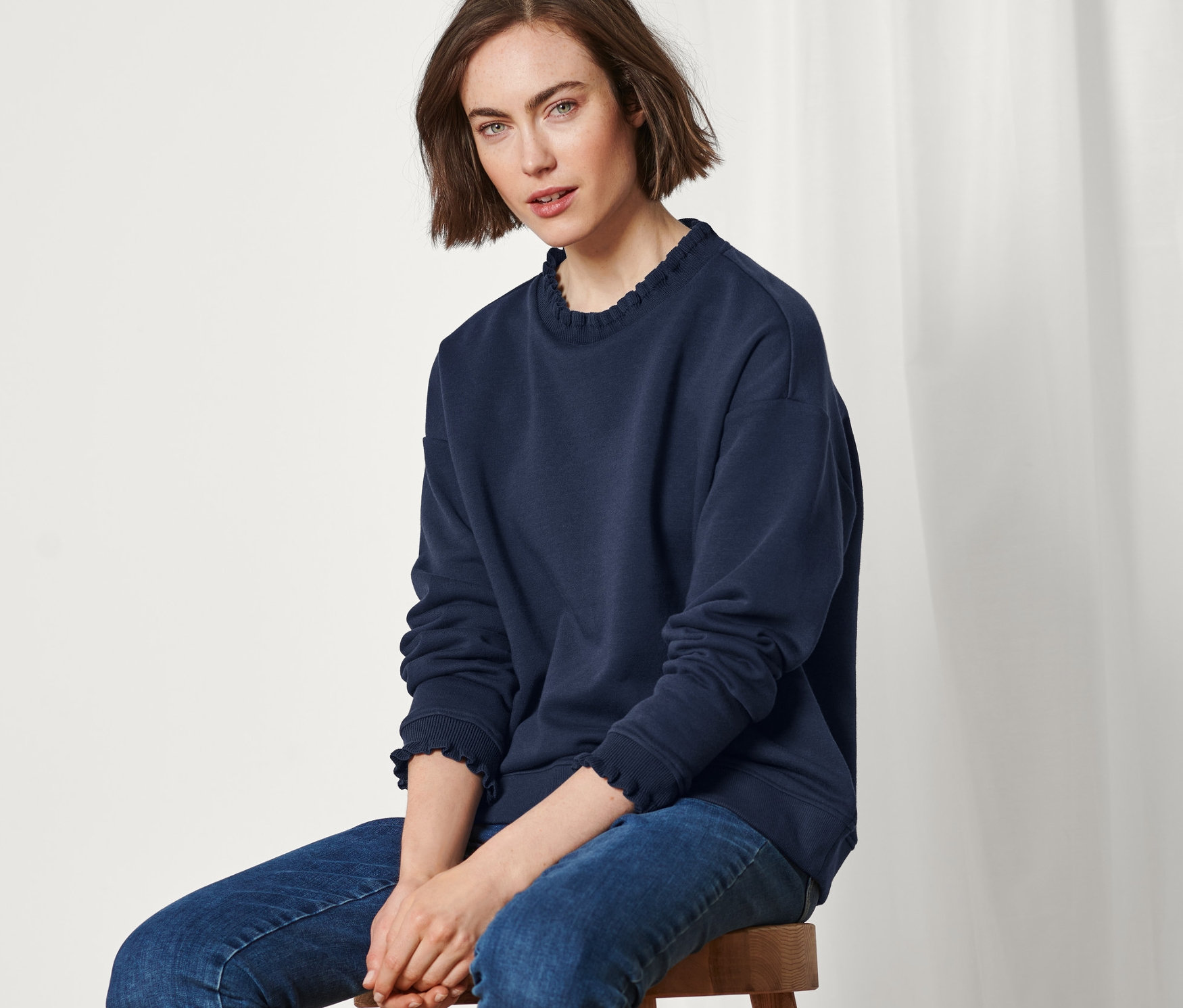 Frau sitzt auf einem Hocker und trägt ein marineblaues Sweatshirt mit Strickdetails.