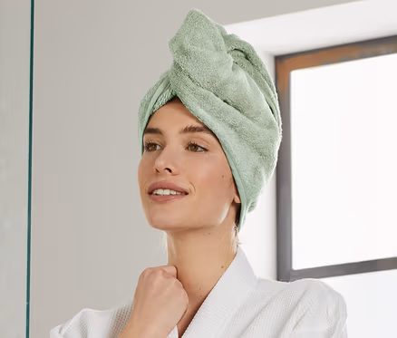 Frau mit grünem Turban-Handtuch und Bademantel im Badezimmer.