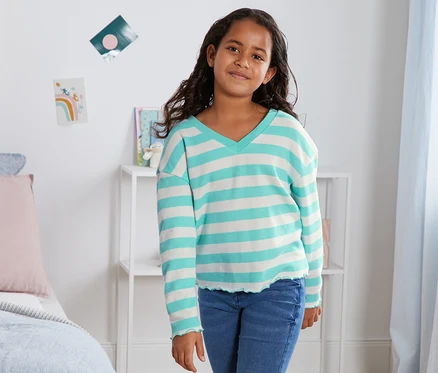 Mädchen posiert in einem blau gestreiften Sweatshirt aus Bio-Baumwolle.