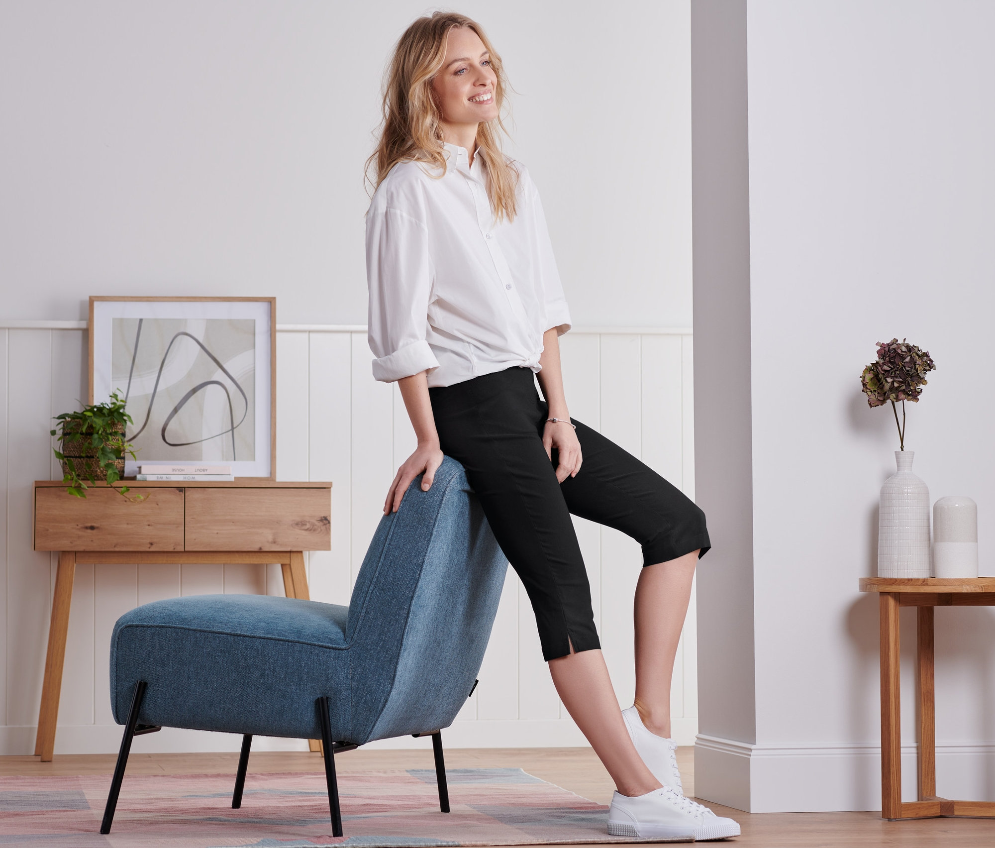 Frau sitzt auf blauem Sessel und trägt eine schwarze 3/4-Bengalin-Hose.