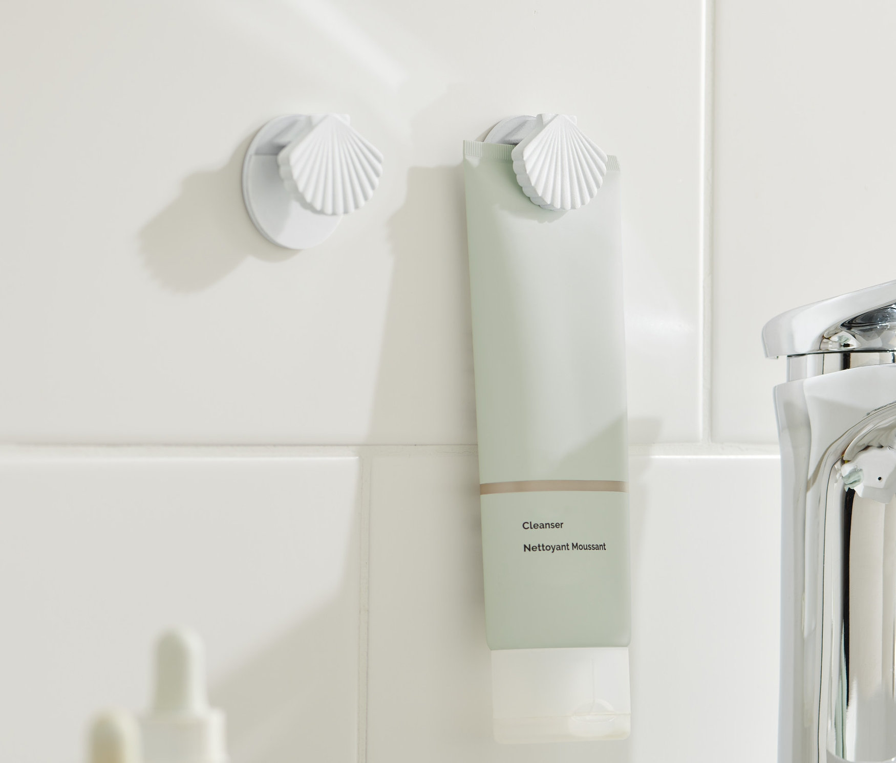 Zwei Tubenhalter sind an weißen Fliesen befestigt, einer davon hält eine grünliche Tube.